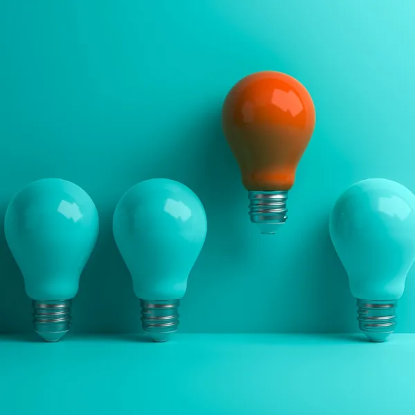One orange light bulb standing out from a row of teal bulbs
